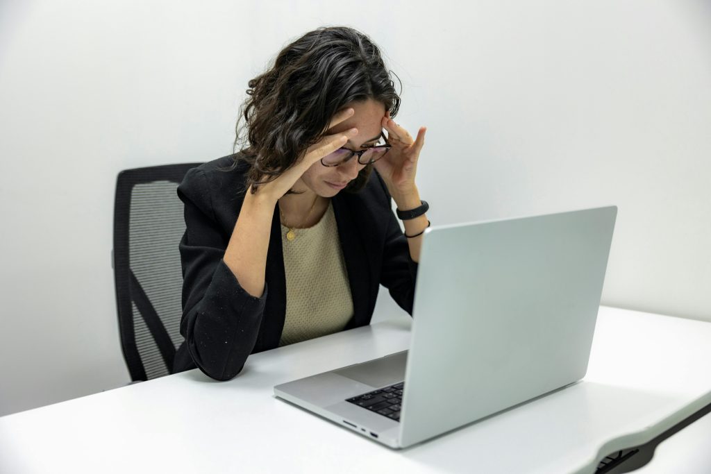 pexels-photo-18848928-18848928 A young woman experiencing stress and fatigue while working on her laptop in an office setting.