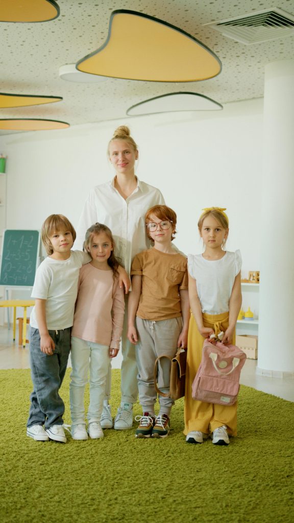 pexels-photo-8088232-8088232 A cheerful teacher with a group of children in a brightly lit classroom, fostering learning.